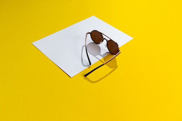 Модные коричневые унисекс стильные круглые очки на белом и желтом фоне абстрактного бумаги, изолированные с копией пространства