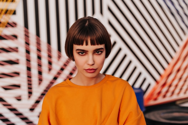 Fashionable brunette lady in orange outfit posing outdoors