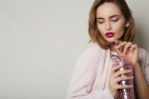 Foto la modella bruna alla moda indossa un maglione rosa, bevendo cocktail in studio. spazio per il testo