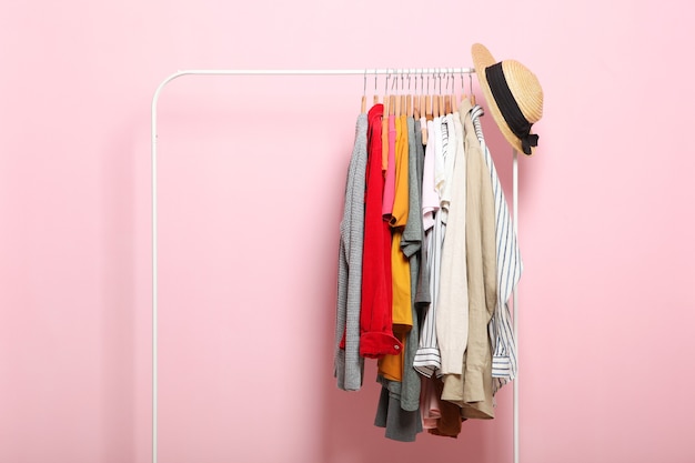 Fashionable clothes on hangers on a wardrobe rack on a colored background