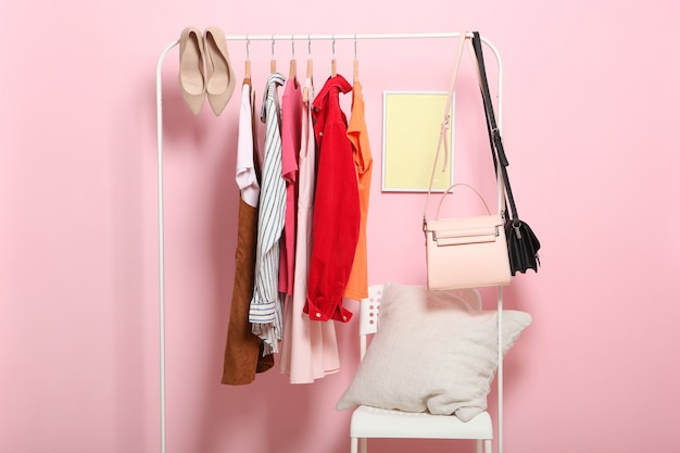 Fashionable clothes on hangers on a wardrobe rack on a colored background