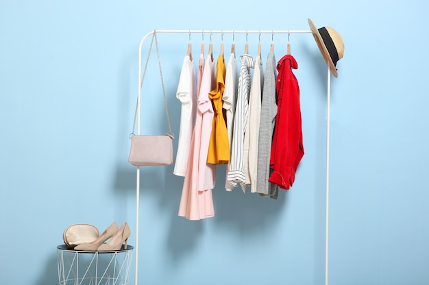 Fashionable clothes on hangers on a wardrobe rack on a colored background