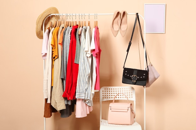 Fashionable clothes on hangers on a wardrobe rack on a colored background