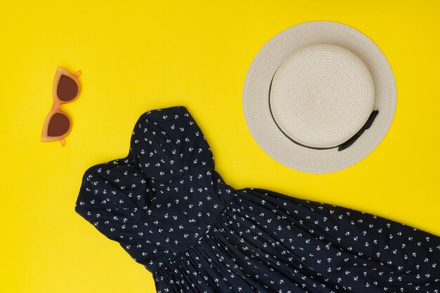 Fashionable concept. Female summer wardrobe. Straw hat, sundress, sunglasses. Yellow background, top view