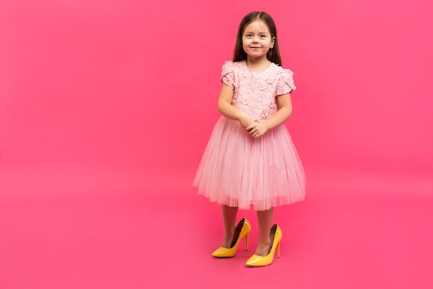 Fashionable cute young girl in big mother's yellow shoes on colored background.