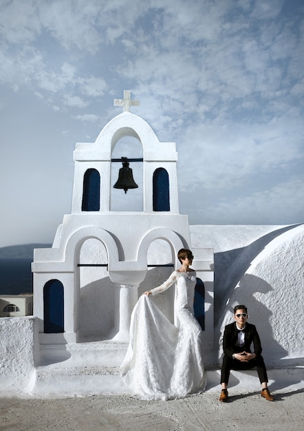 Fashionable elegant newlywed couple at the old white church in the village of Oia on the island of Santorini, Greece