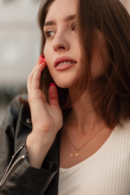 Fashionable female portrait of a beautiful girl with a pretty face and dental braces in a fashion black leather jacket and white dress in the city