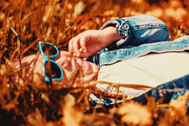 ファッショナブルな女の子は草の中に横たわって笑います。幸せな子供時代。高品質の写真