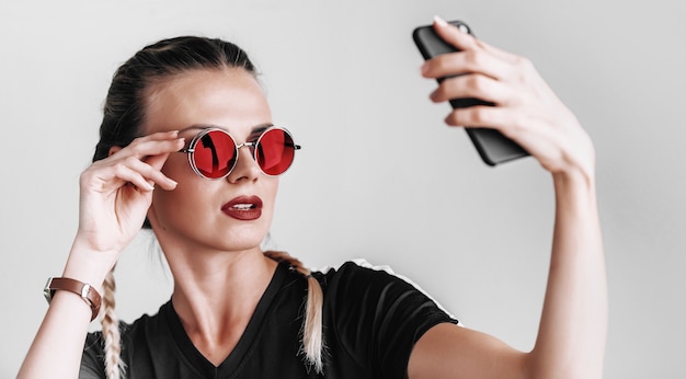 Fashionable girl in sunglasses with colored glasses does selfie on the phone