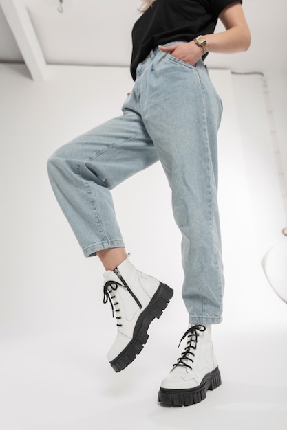 Fashionable girl in vintage wide blue jeans with stylish white boots poses in the studio Female legs with leather shoes