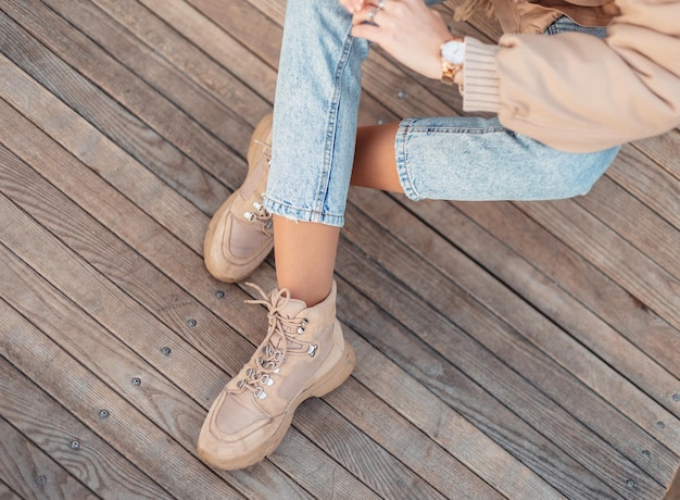 Ragazza alla moda con capispalla invernali alla moda in jeans classici blu e scarpe beige in pelle alla moda si siede su un pavimento in legno vintage