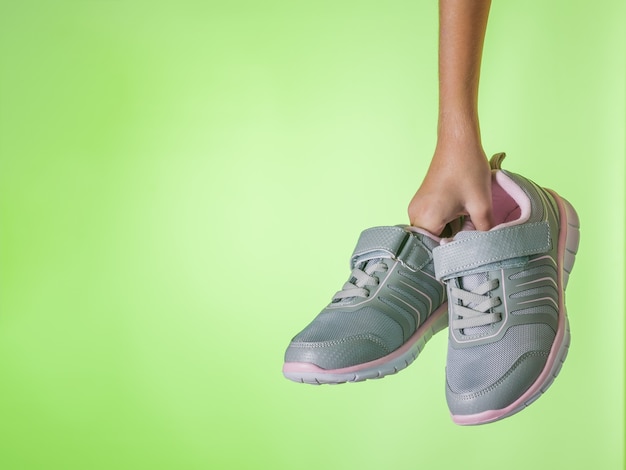 Fashionable gray sneakers in a child's hand on a green background. Sports shoes. Color trend. Space for your text.