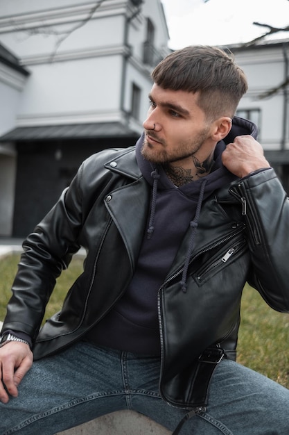 Premium Photo | Fashionable handsome man with hair and a beard with a  tattoo on his neck in fashionable casual outfit with a hoodie and a jacket  sits on the street