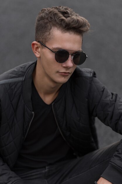 Fashionable handsome young man with stylish vintage sunglasses and black trendy jacket in the street