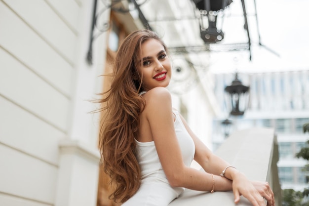 Fashionable happy young beauty elegant woman with smile with red lips in white trendy dress outdoors Fresh adorable pretty lady