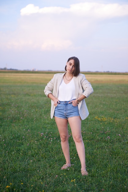 Fashionable hipster posing outside in a beige jacket and a jeans shorts