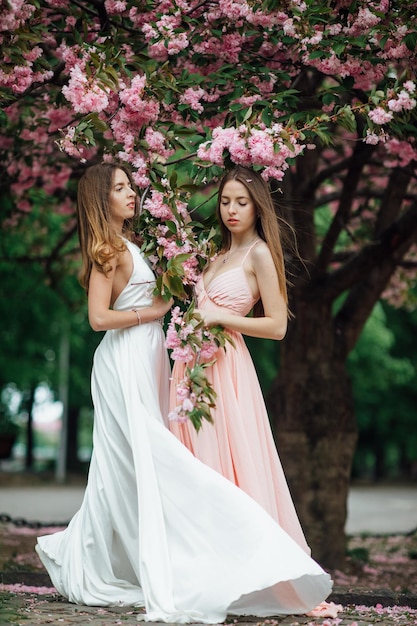 ファッショナブルな女性が花の木の近くでポーズをとっています。ツインガールズウィメンズの美しさとファッション。