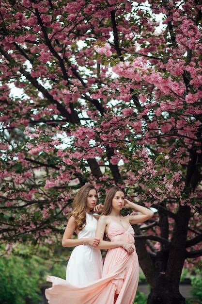 Модница позирует возле цветущего дерева. Twin Girls Женская красота и мода.