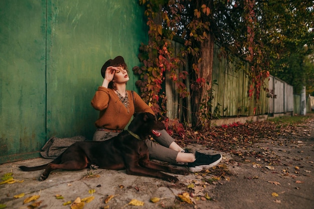 Fashionable lady sits outside in autumn day near country house and looks away against the backdrop of beautiful autumn countryside landscape Copy space