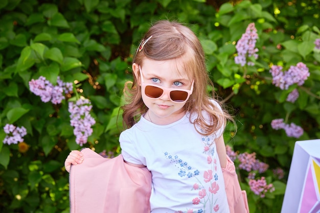 Fashionable little girl in sunglasses walks through a blooming garden