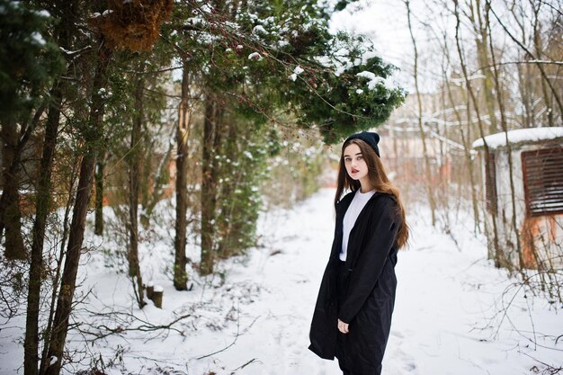 Модная модель брюнетки с длинными ногами в длинном черном плаще и шляпе на открытом воздухе в зимний день.