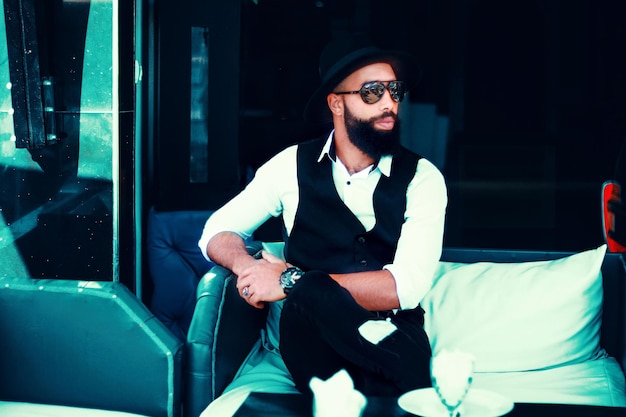 Photo fashionable man in sunglasses sitting on sofa at restaurant