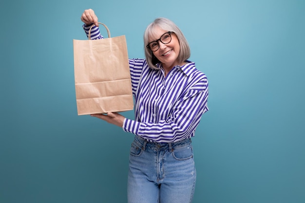 Fashionable middleaged woman with gray hair holding out a package with social assistance on a bright