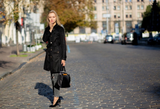 Fashionable model with long hair wearing trench coat and torn jeans, posing with sun light