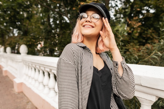 Fashionable portrait of beautiful teenager girl model in glasses with a stylish plaid shirt and t-shirt walks in the park