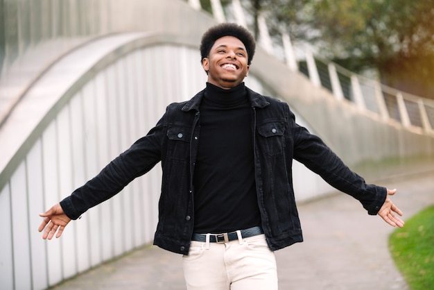 Fashionable portrait of a handsome Moroccan man with afro hair with his arms open looking up very smiling and happy with urban style clothes