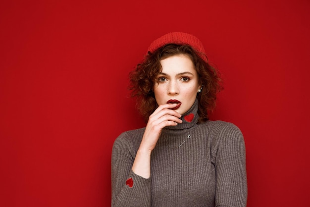 Fashionable portrait of a young model in a hat and gray sweater with curly hair