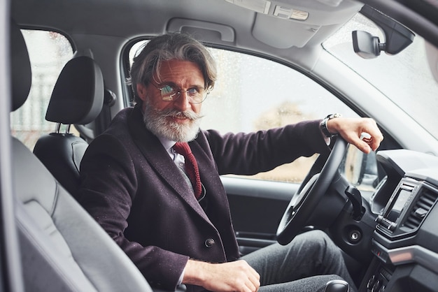 L'uomo anziano alla moda in abiti eleganti è nell'auto moderna.