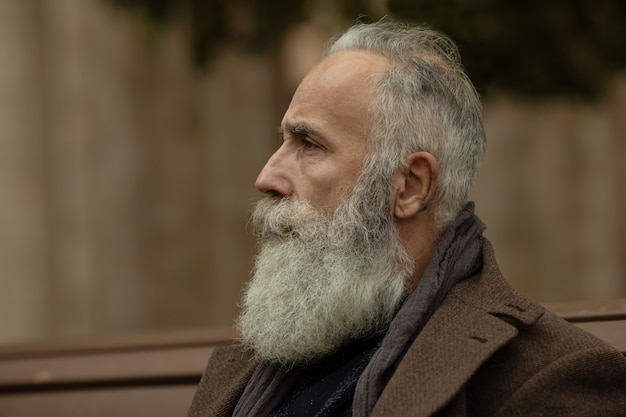Фото Модный старший мужчина с седыми волосами и бородой находится на улице на улице.