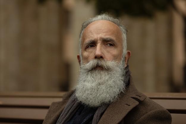 Fashionable senior man with gray hair and beard is outdoors on the street.