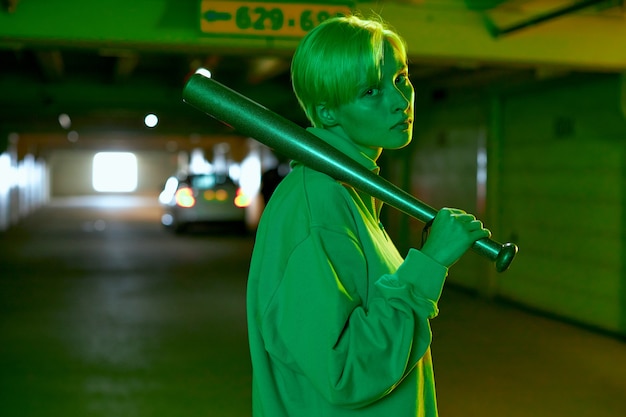 사진 주차장에 서 있는 박쥐를 들고 짧은 머리를 가진 네온 녹색 불빛 소녀의 세련된 촬영 ...