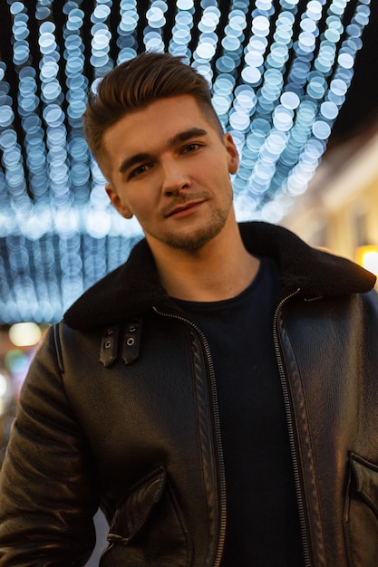 Fashionable street portrait of a handsome stylish professional man with leather jacket hair walking in the night city with blue lights