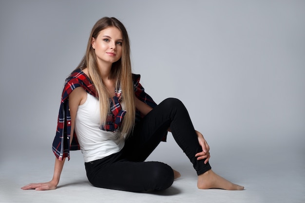 Fashionable studio portrait of a beautiful girl in a plaid shirt on a gray wall