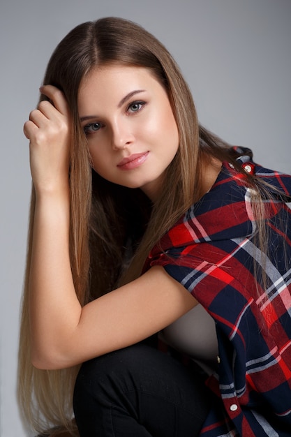 Fashionable studio portrait of a beautiful girl in a plaid shirt on a gray wall