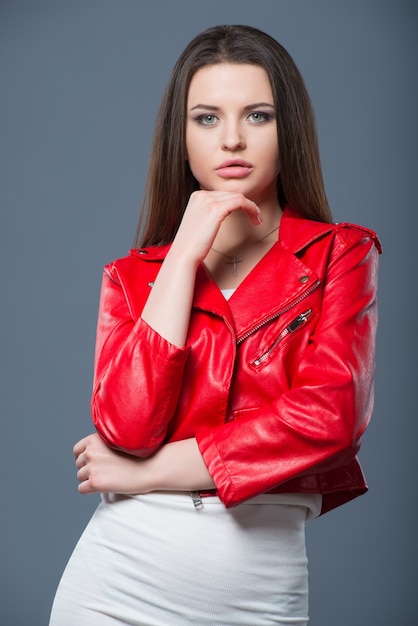 Fashionable style, fashion women's clothing, color combination. Beautiful brunette girl in white dress and red leather jacket isolated gray background.