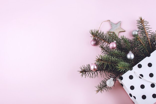 Fashionable stylish Christmas composition with gift bag, fir branches and toy presents on pastel background