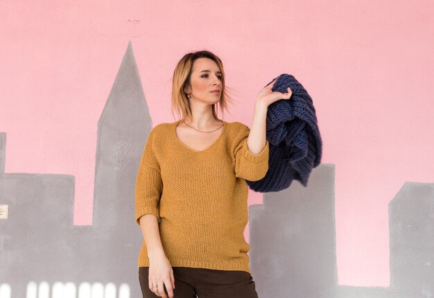 A fashionable and stylish girl in fashionable vintage clothes with a handbag poses against the wall.