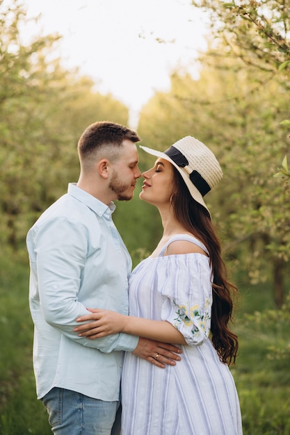 Fashionable and stylish happy pregnant woman and her husband dressed a pastel white and blue tone in the garden on the sunset