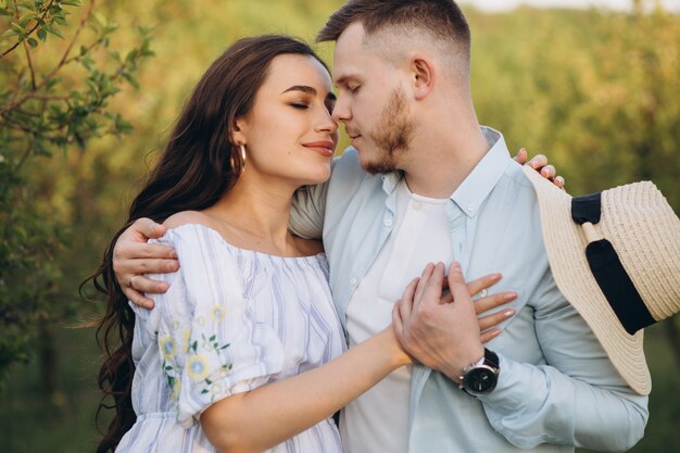 Fashionable and stylish happy pregnant woman and her husband dressed a pastel white and blue tone in the garden on the sunset