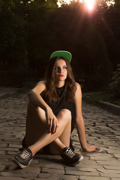 Fashionable stylish young woman in sport apparel sitting on the cobbles at the evening