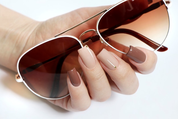 Fashionable sun glasses and stylish manicure in beige brown nail polish colors