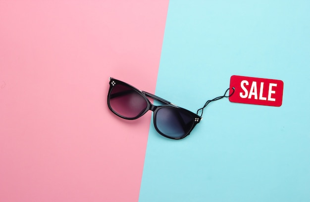 Fashionable sunglasses with red sale tag on pink blue pastel.