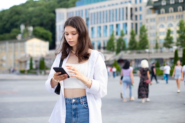 Модная девочка-подросток в повседневной одежде с помощью телефона, стоя посреди улицы. Всемирный день туризма