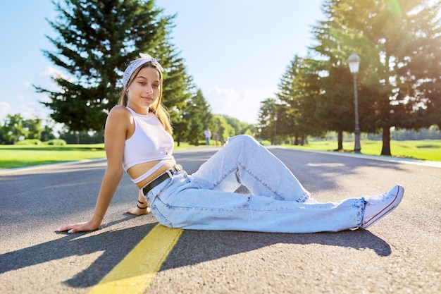 Fashionable teenage girl posing sitting on the road in park