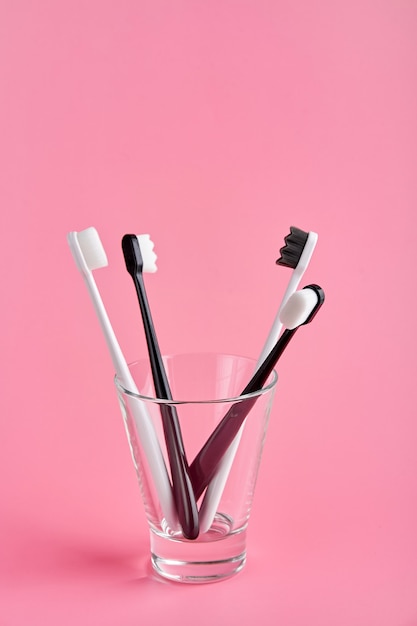 Fashionable toothbrush with soft bristles. Popular toothbrushes. Hygiene trends. Kit of toothbrushes in glass on pink background.