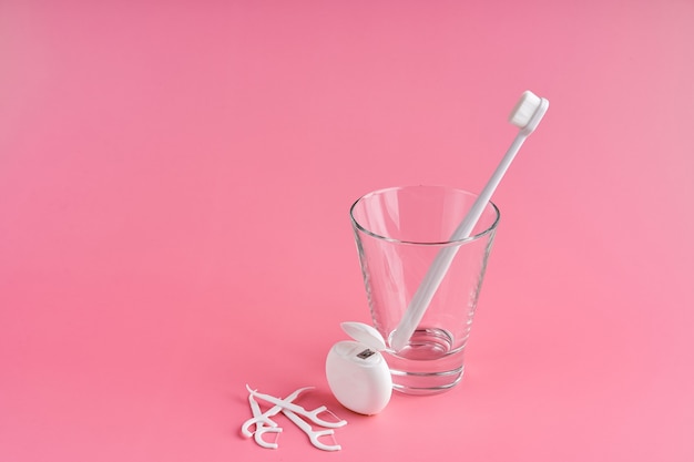 Fashionable toothbrush with soft bristles. Popular toothbrushes. Hygiene trends. Oral hygiene kit. Toothbrushes in glass, floss thread and toothpicks on a pink background.